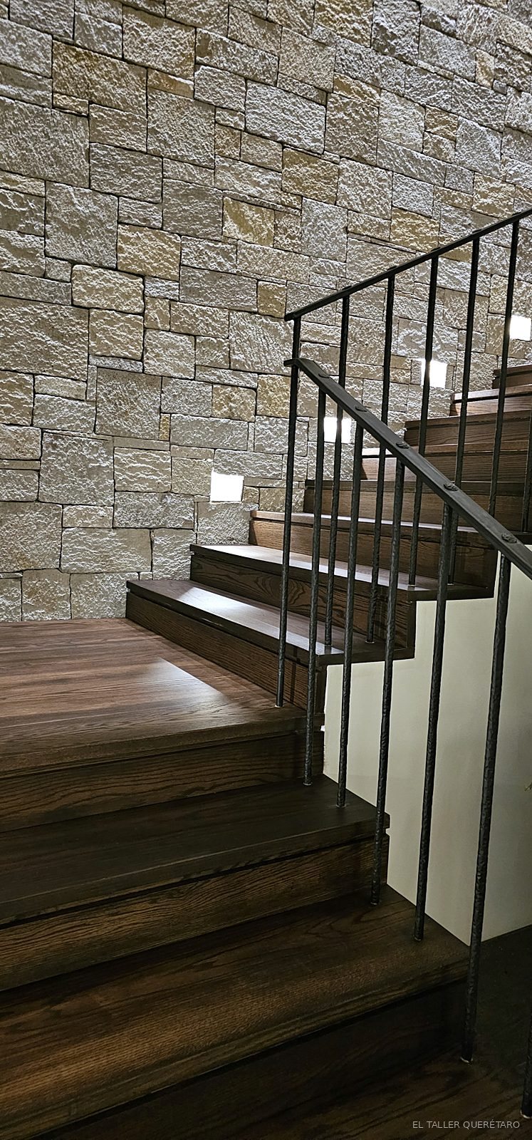 Escalera de madera con muro de piedra y barandal de herrería