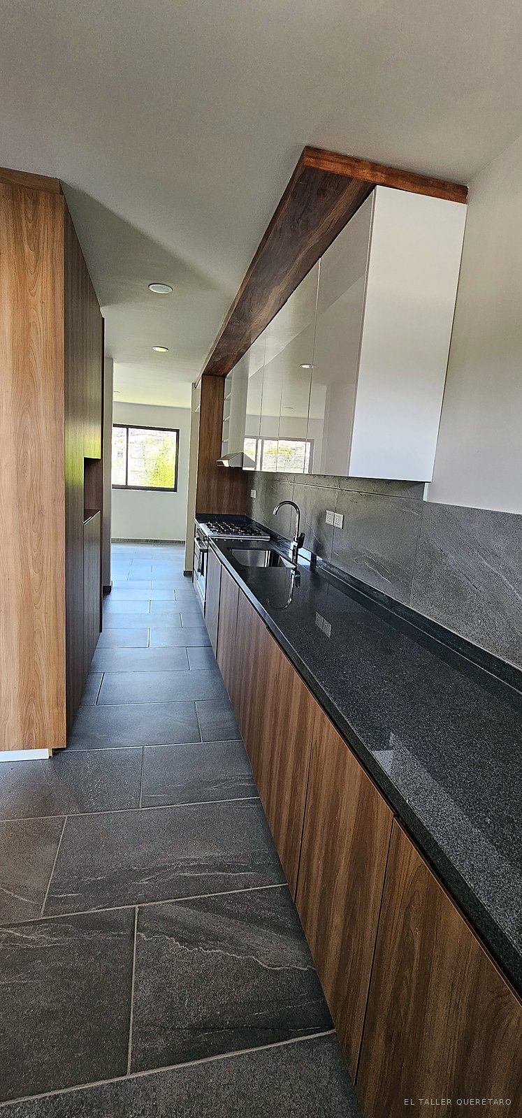Cocina lineal con alacena alta enmarcada en madera y cubierta de granito