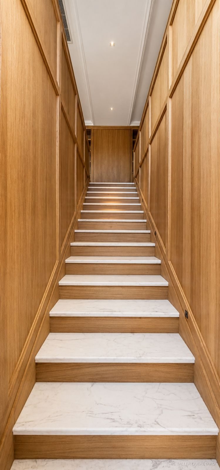 Escalera con muros forrados en roble europeo y huellas de mármol