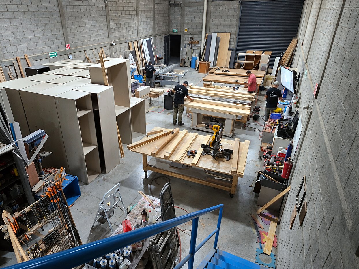 Interior de El Taller en Querétaro visto desde arriba: mesas de trabajo, módulos armados y el equipo preparando madera